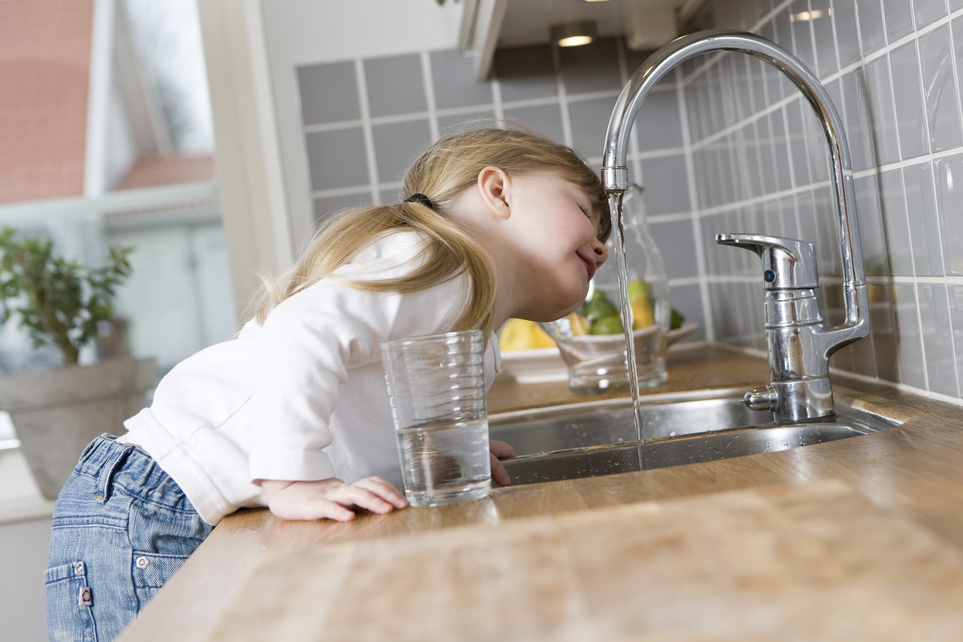 Little girl in the kitchen drinking water from the tap