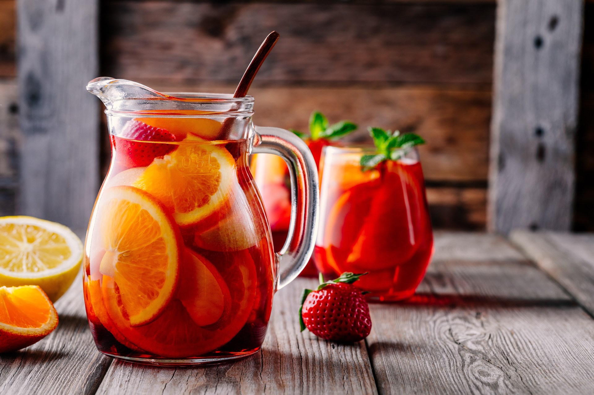 Homemade red wine sangria with orange, apple, strawberry and ice in pitcher and glass on rustic wooden background