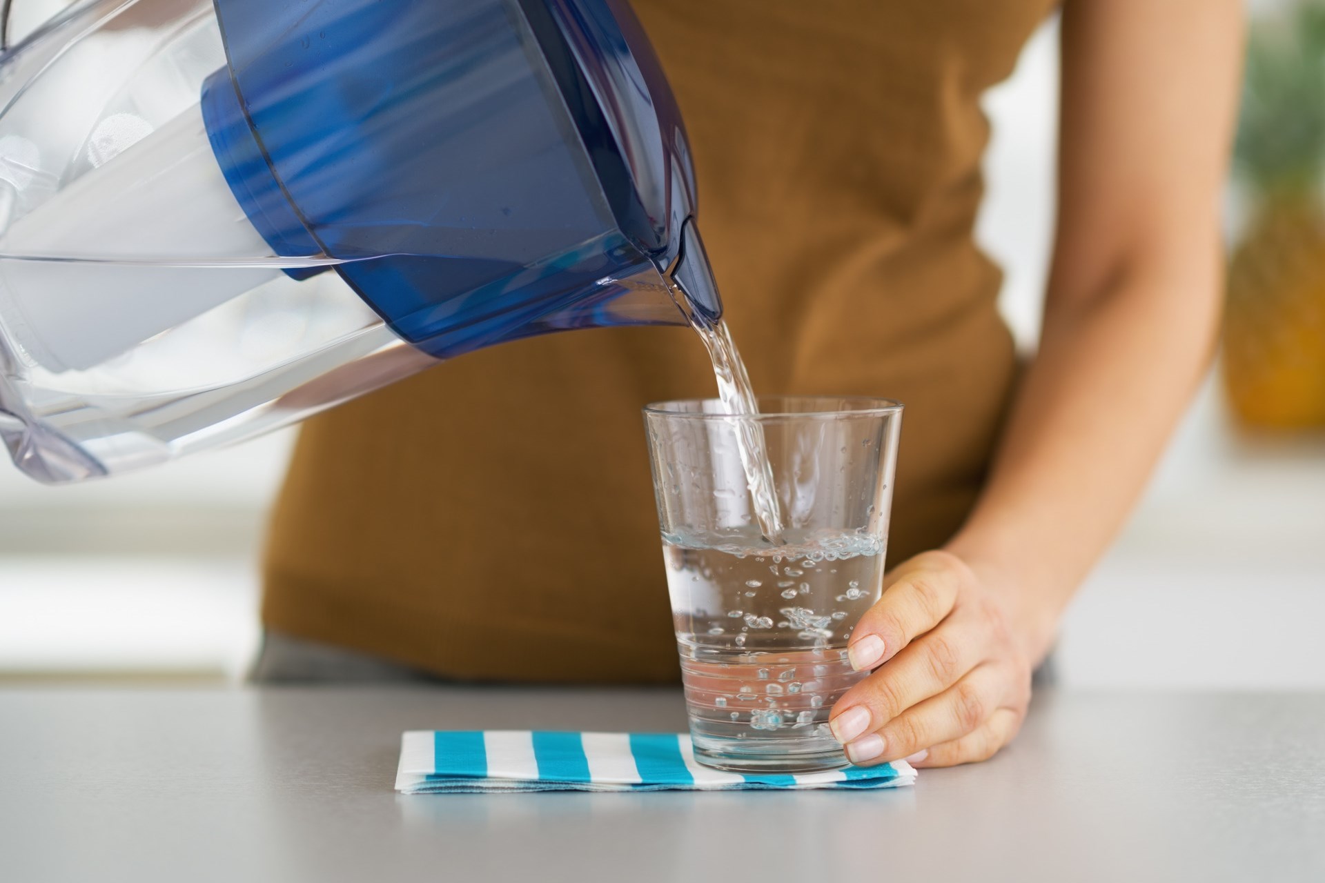 Closeup on housewife pouring water into glass from water filter pitcher