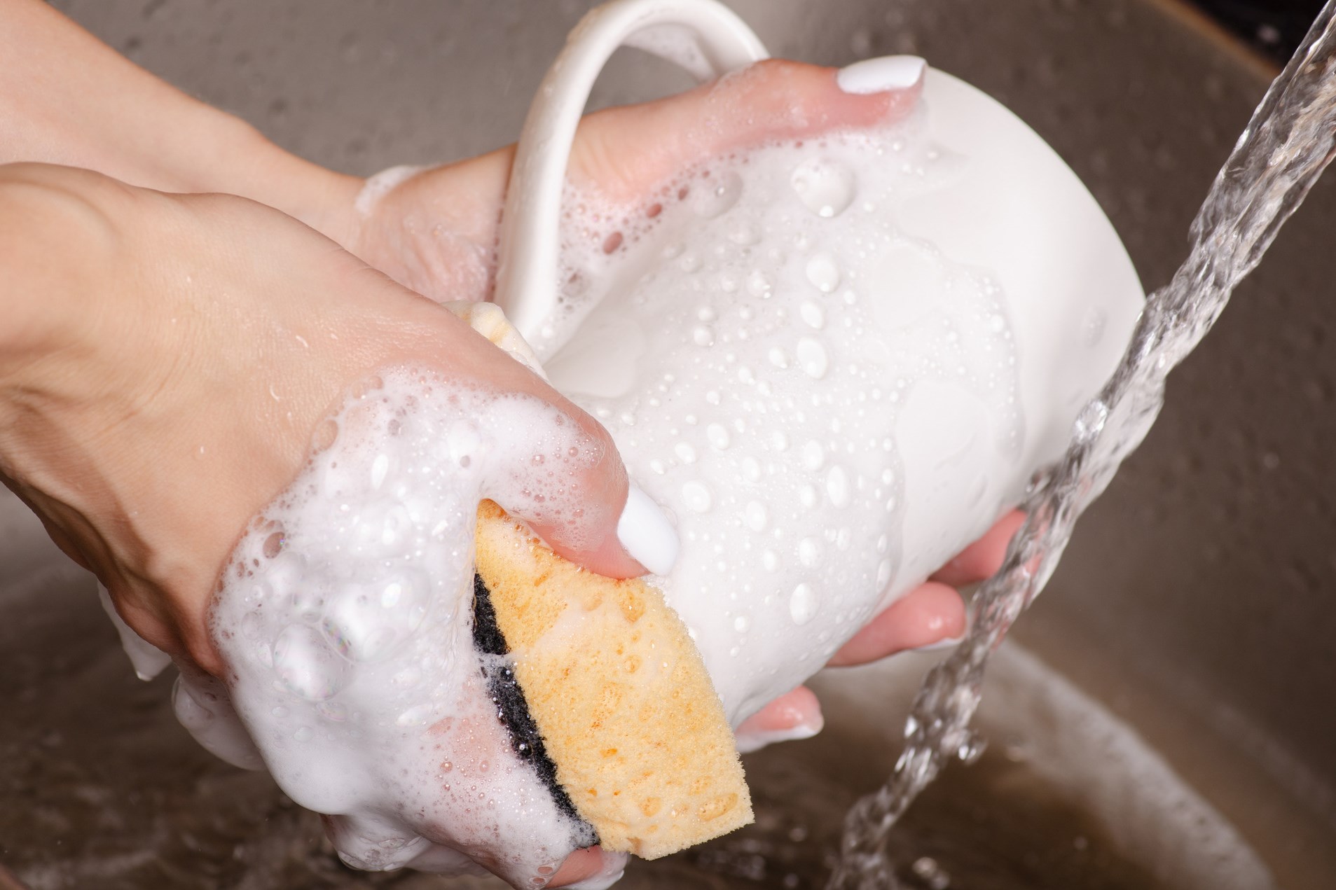 A woman washes a cup with a lot of foam and water.