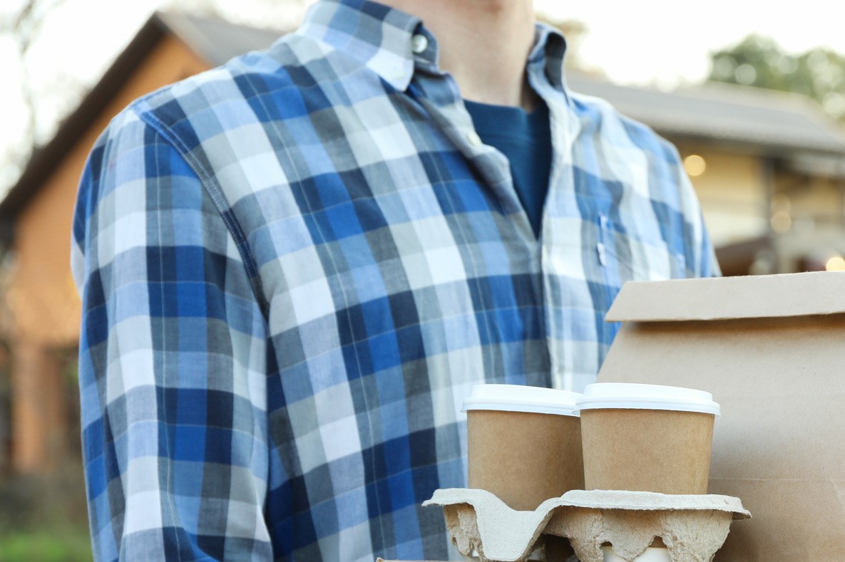 Man holds blank box, coffee cups and paper package outdoor.