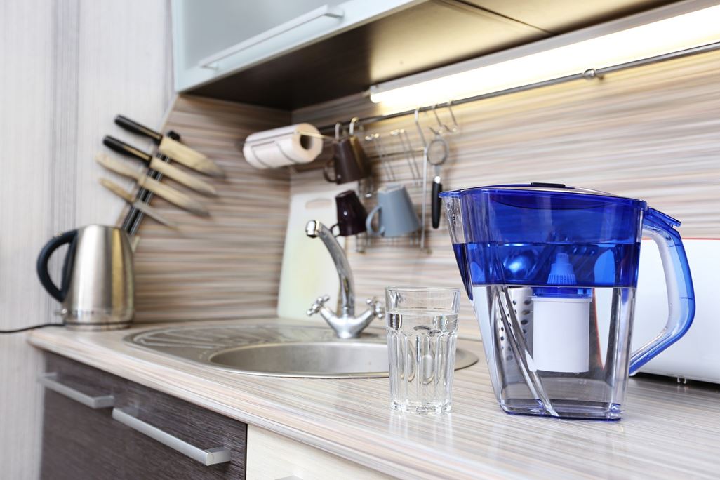 Glass of clean water and filter for cleaning drinking water on the table in the kitchen. Purification of drinking water at home.