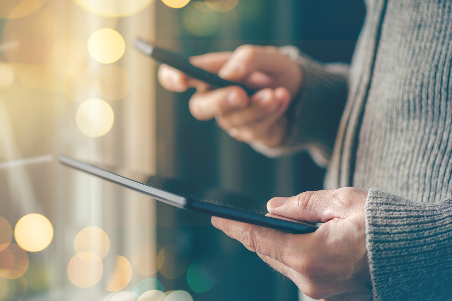 Smartphone and tablet data synchronization, man syncing files and documents on personal wireless electronic devices at home, selective focus with shallow depth of field and bokeh light.