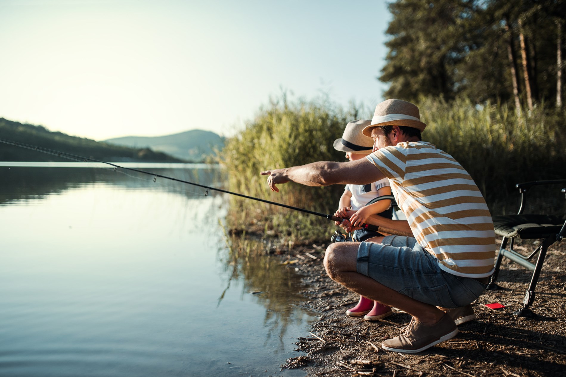 A mature father with a small toddler son outdoors fishing by a lake.