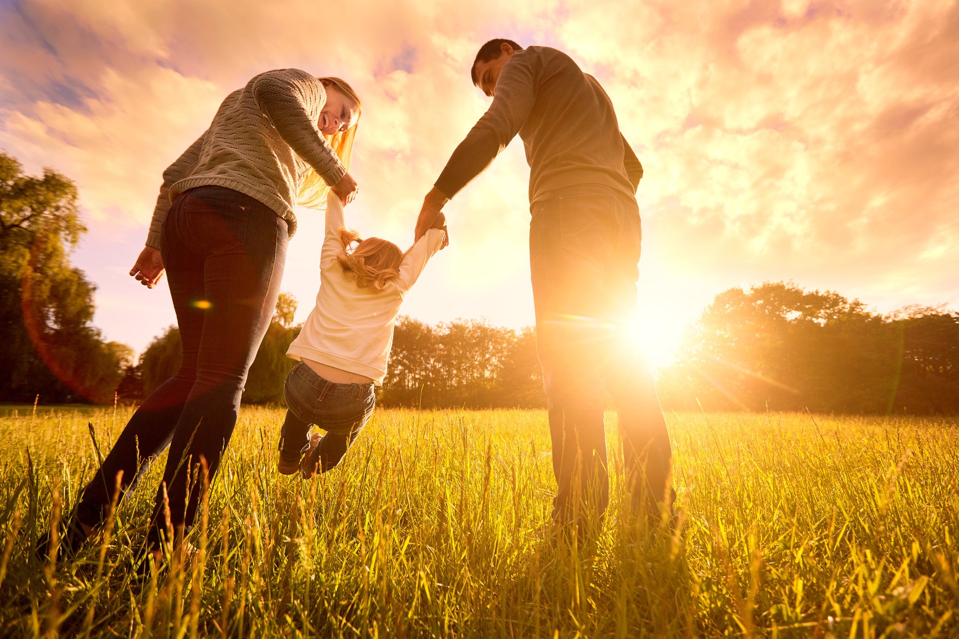Happy family in the park evening light. The lights of a sun. Mom, dad and baby happy walk at sunset. The concept of a happy family.Parents hold the baby&amp;#39;s hands.