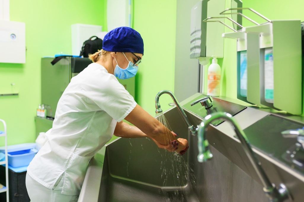Female Surgeon in a medical mask and in a suit in the hospital washing thoroughly her hands before performing a surgery