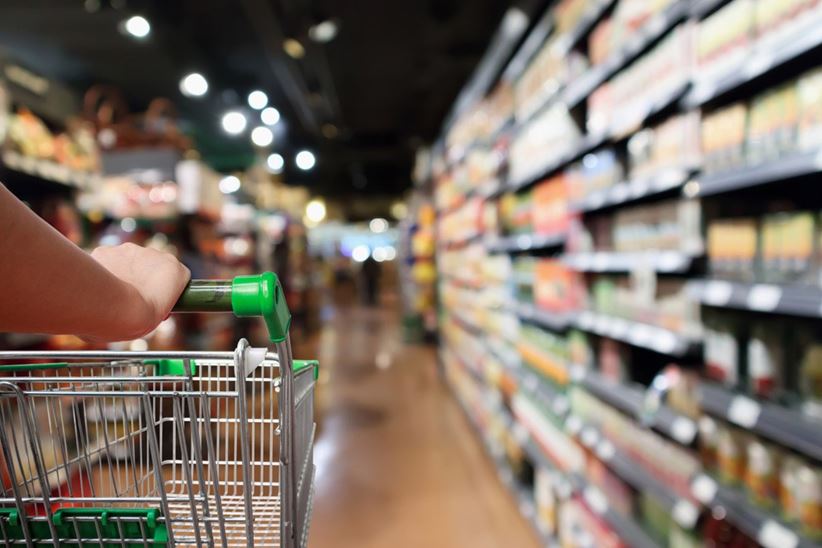 Woman hand hold shopping cart with blur supermarket aisle background