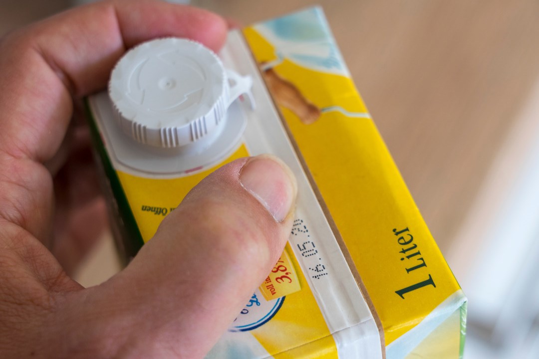Hand opens 1 liter milk carton with visible best before date.