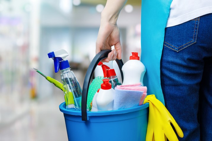 Eine Putzfrau steht im Inneren eines Gebäudes und hält einen mit Chemikalien gefüllten Eimer in der Hand.