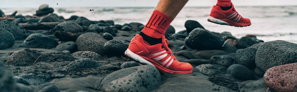 Laufschuhe des Sportlers Mann joggt am Strand. Schwieriges Terrain mit nassen Felsen für das Training im Freien. Läufer beim Training.