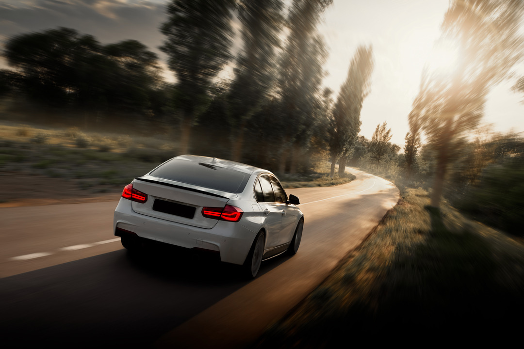 White car is driving on empty countryside asphalt road at sunset