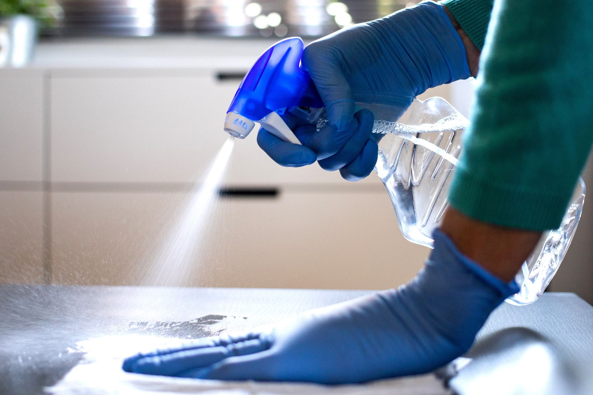 Surface home cleaning spraying antibacterial sanitizing spray bottle disinfecting against COVID-19 spreading wearing medical blue gloves. Sanitize surfaces prevention in hospitals and public spaces.