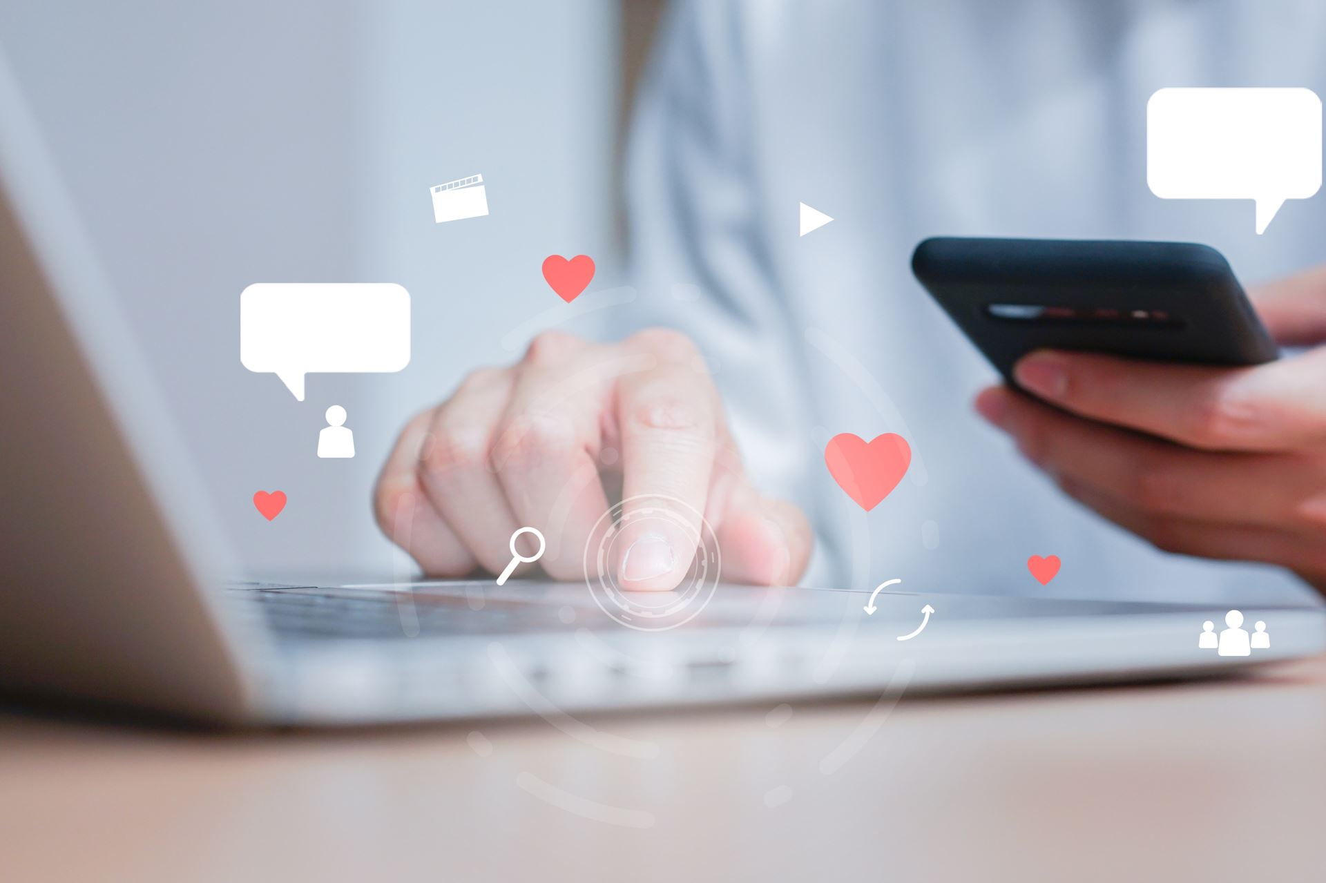 Hands with handheld and typing on laptop keyboard, with chat boxes and hearts as visualization.