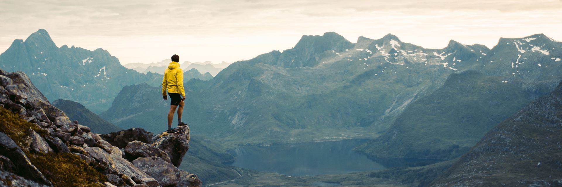 Man on a mountain overlooking the valley; cloudy sky.
