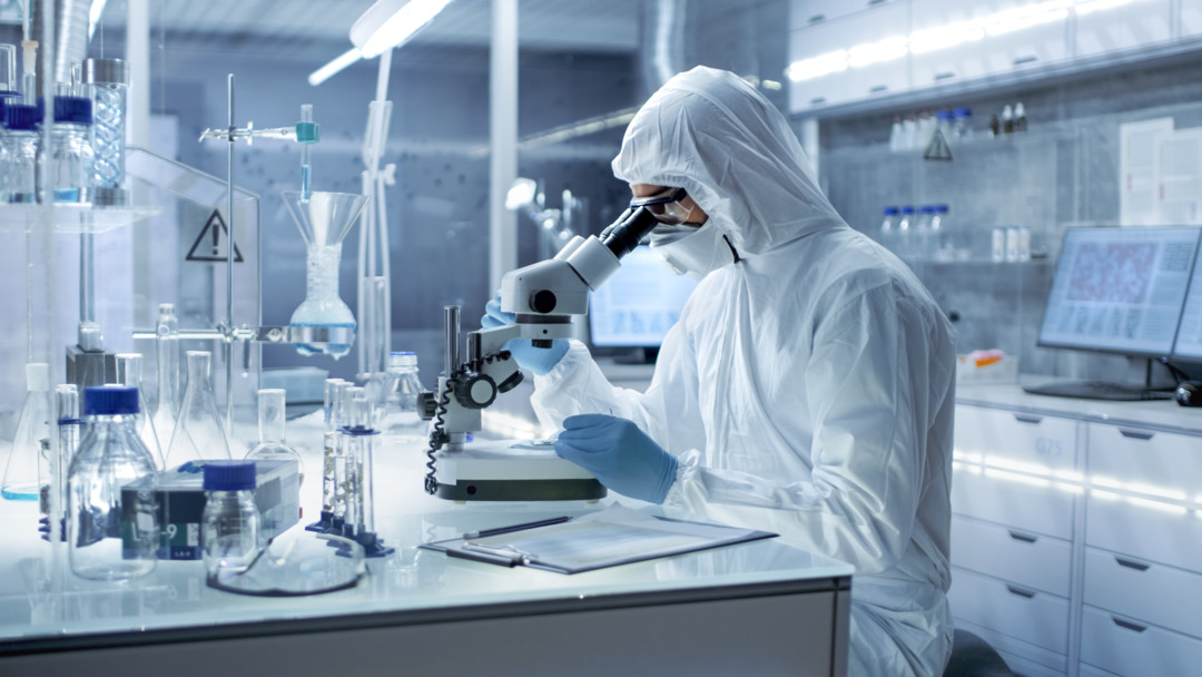 In a Secure High Level Research Laboratory Scientist in a Coverall Examines Petri Dish Under Microscope.