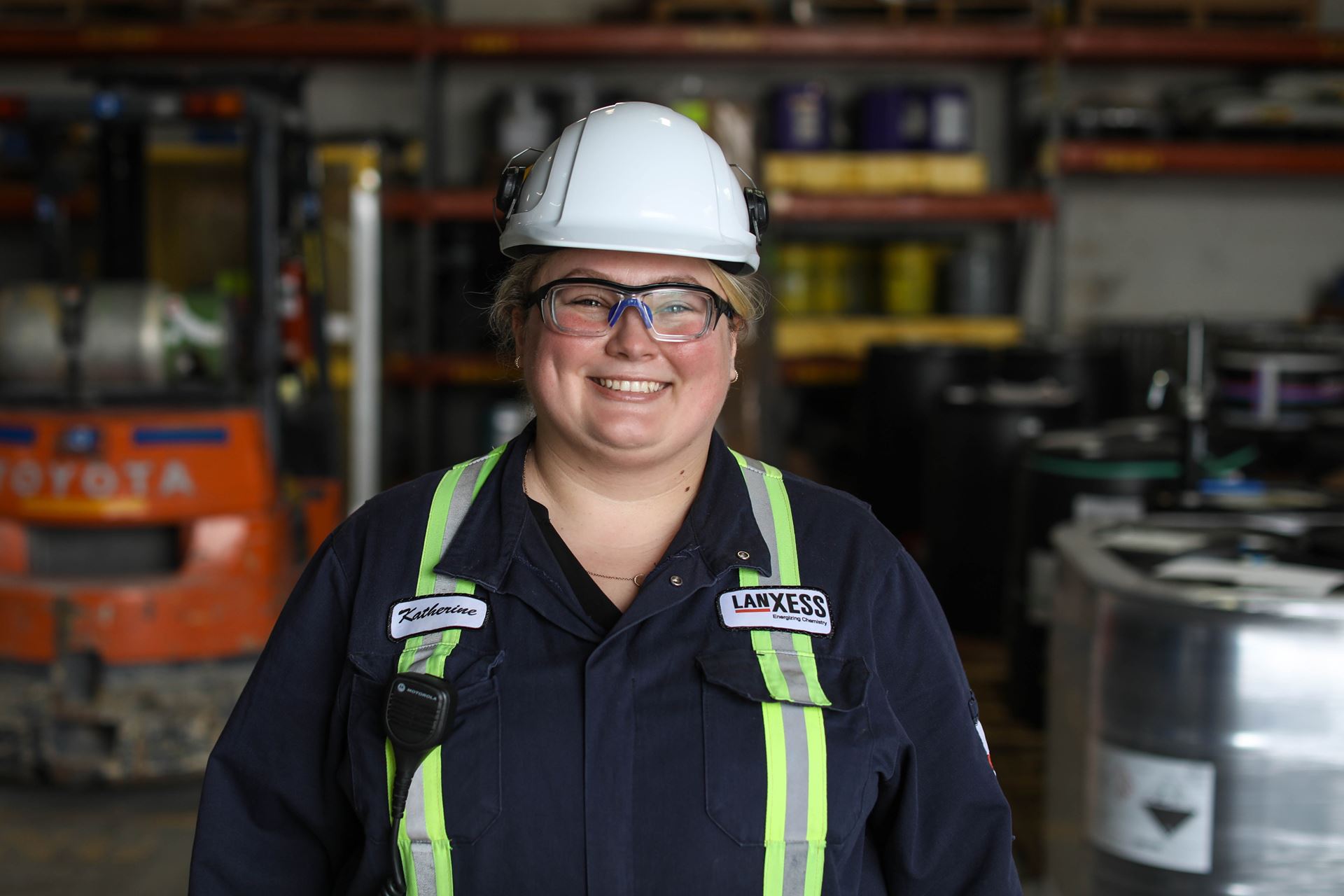Katherine Down stands in the production area wearing a helmet, protection glasses and smiling.