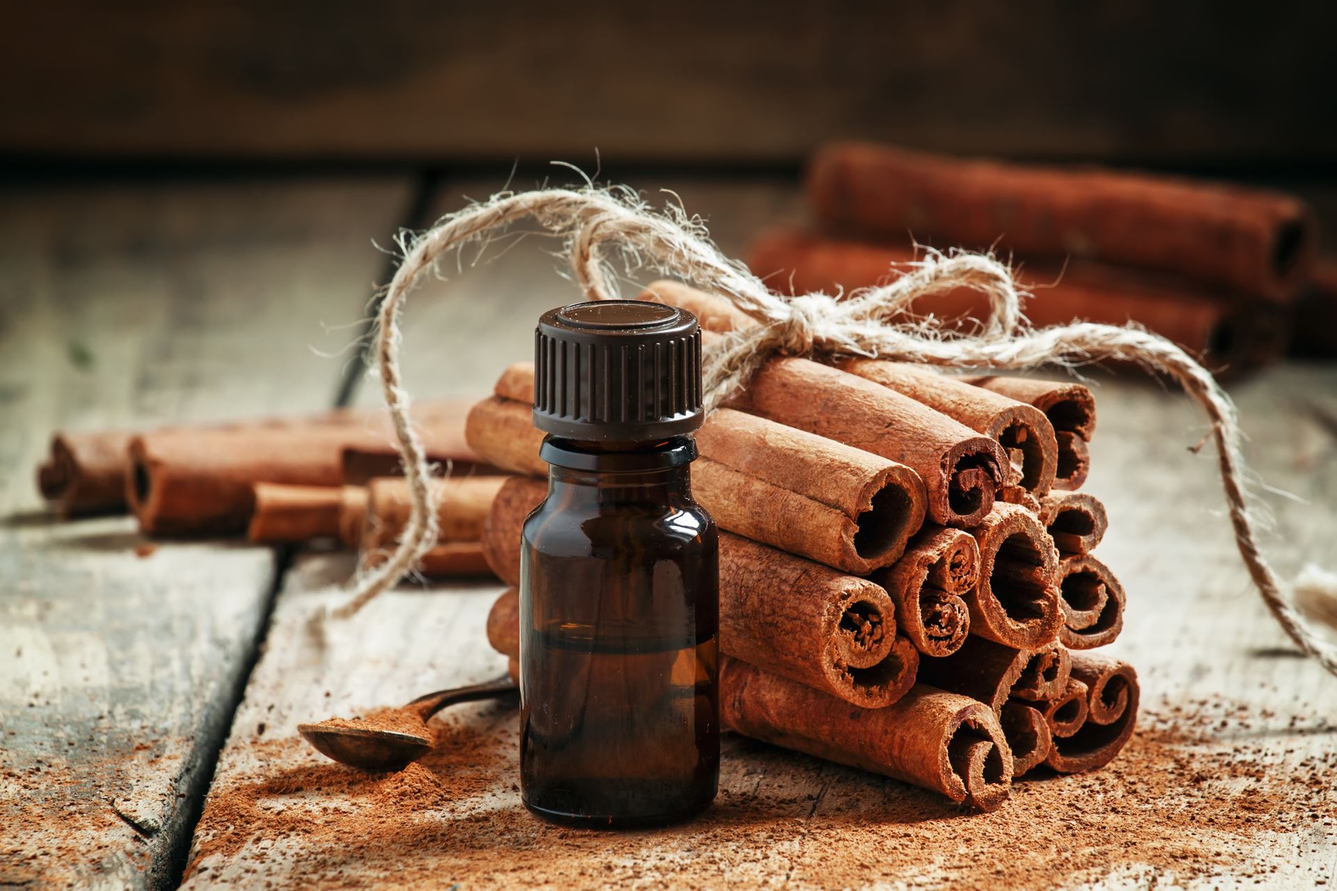 Essential cinnamon oil in a small bottle, ground cinnamon and cinnamon sticks on old wooden background, selective focus