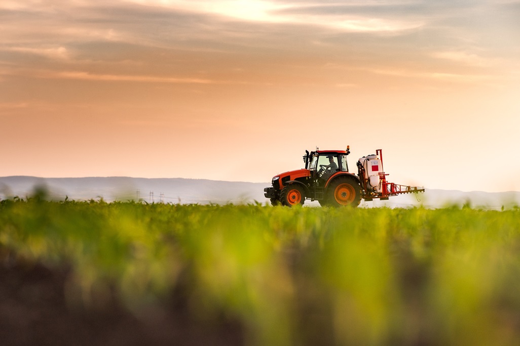 Tractor spraying corn field in sunset