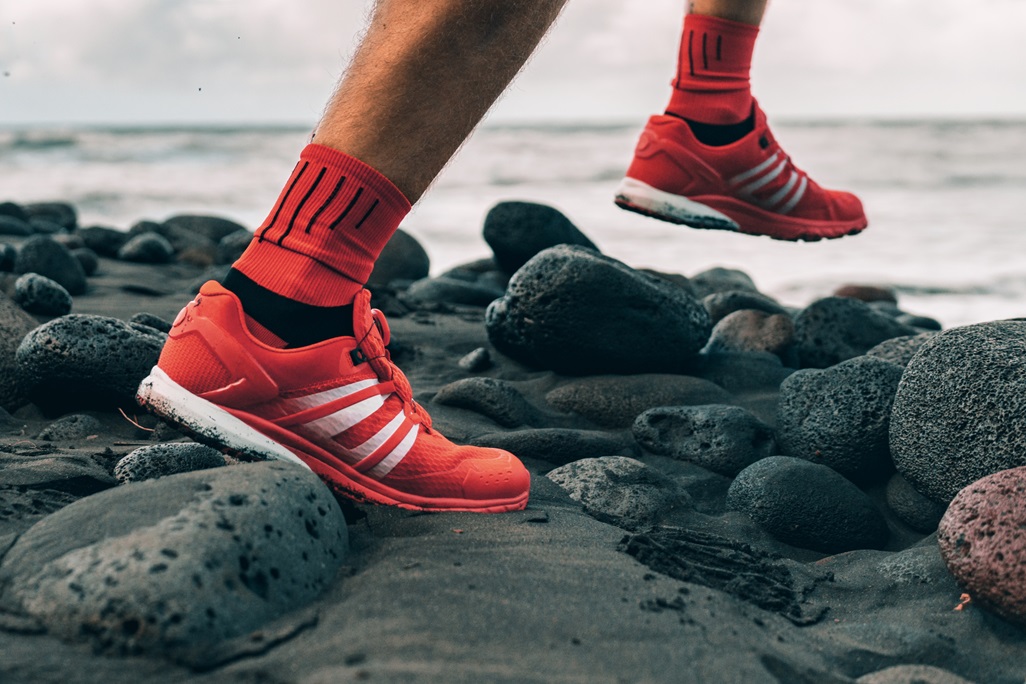 Running shoes of athlete man jogging on beach. Difficult terrain with wet rocks for training outdoors. Runner exercising.