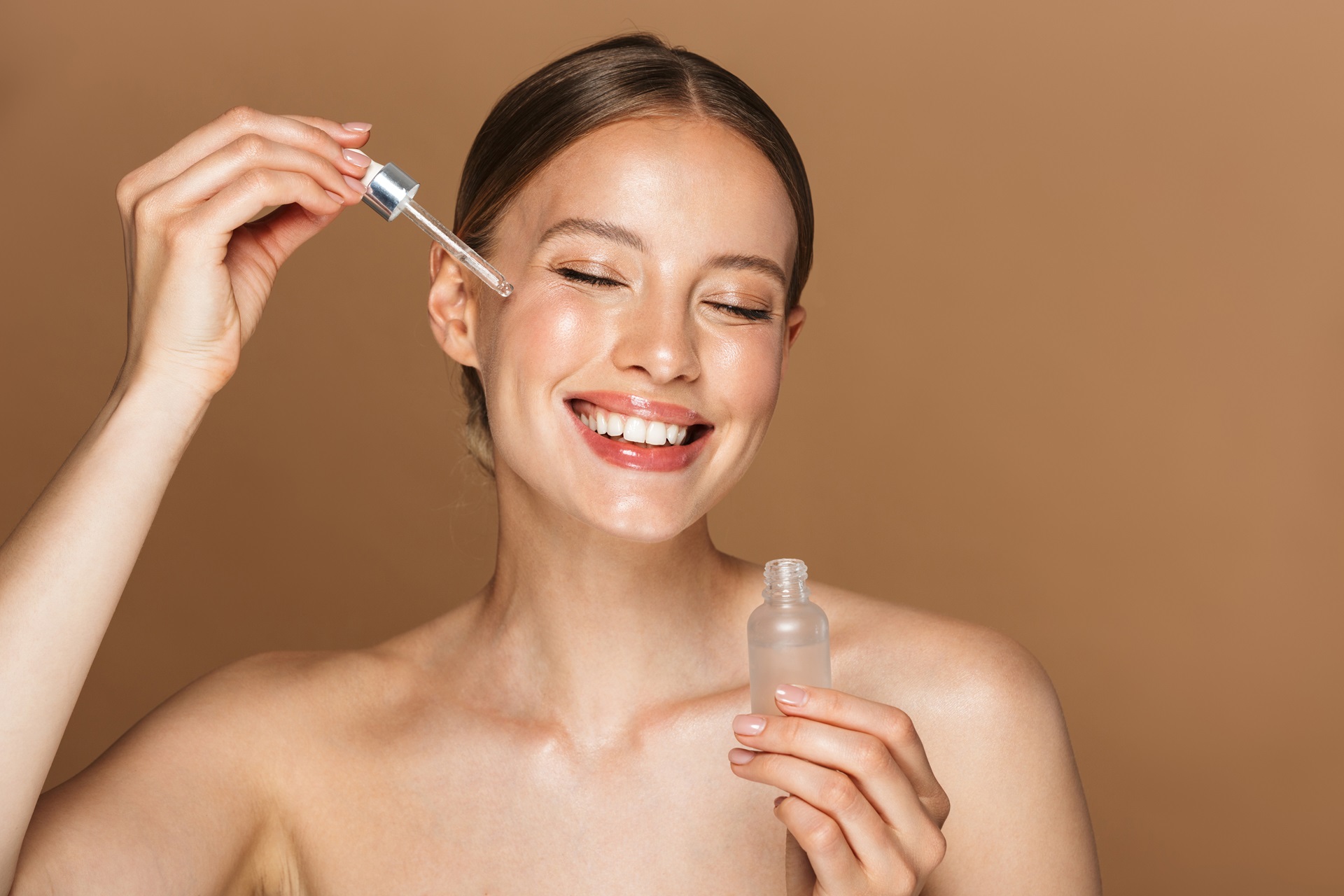 Beautiful happy young amazing woman posing isolated over brown chocolate background wall holding oil drop serum.