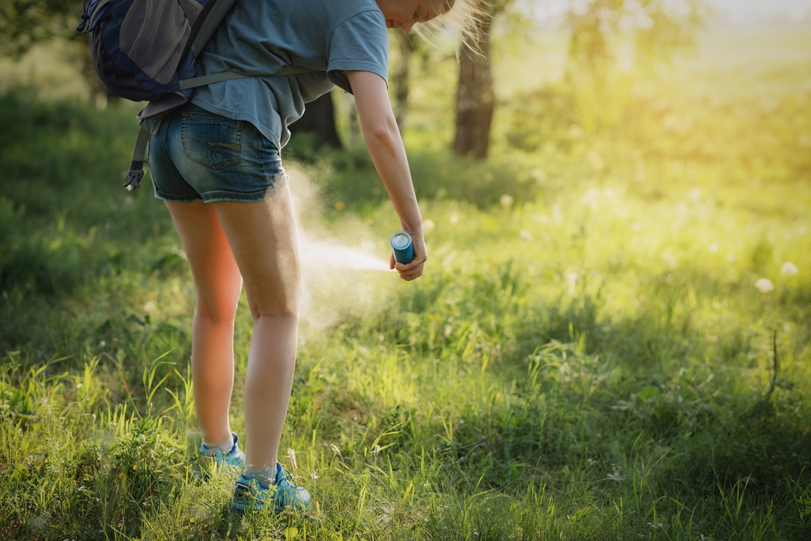 Wanderer trägt im Wald Mückenschutzmittel auf die Haut der Beine auf.